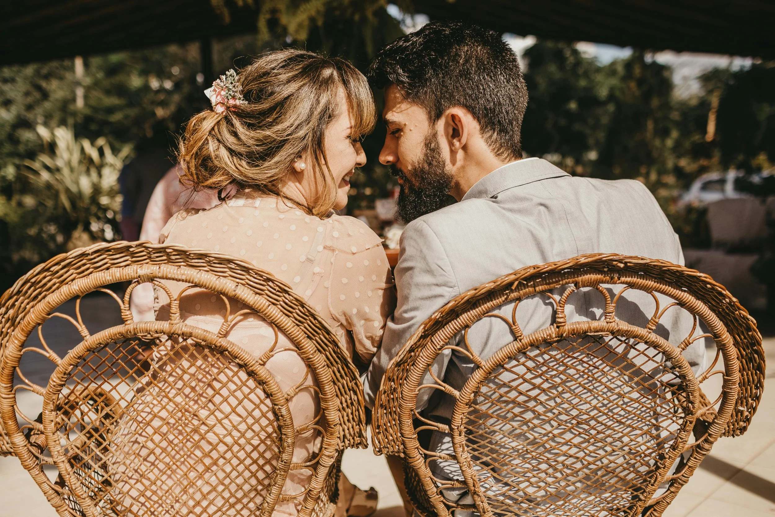 a man and woman are seated in wicker chairs next to each other, looking at each other tenderly