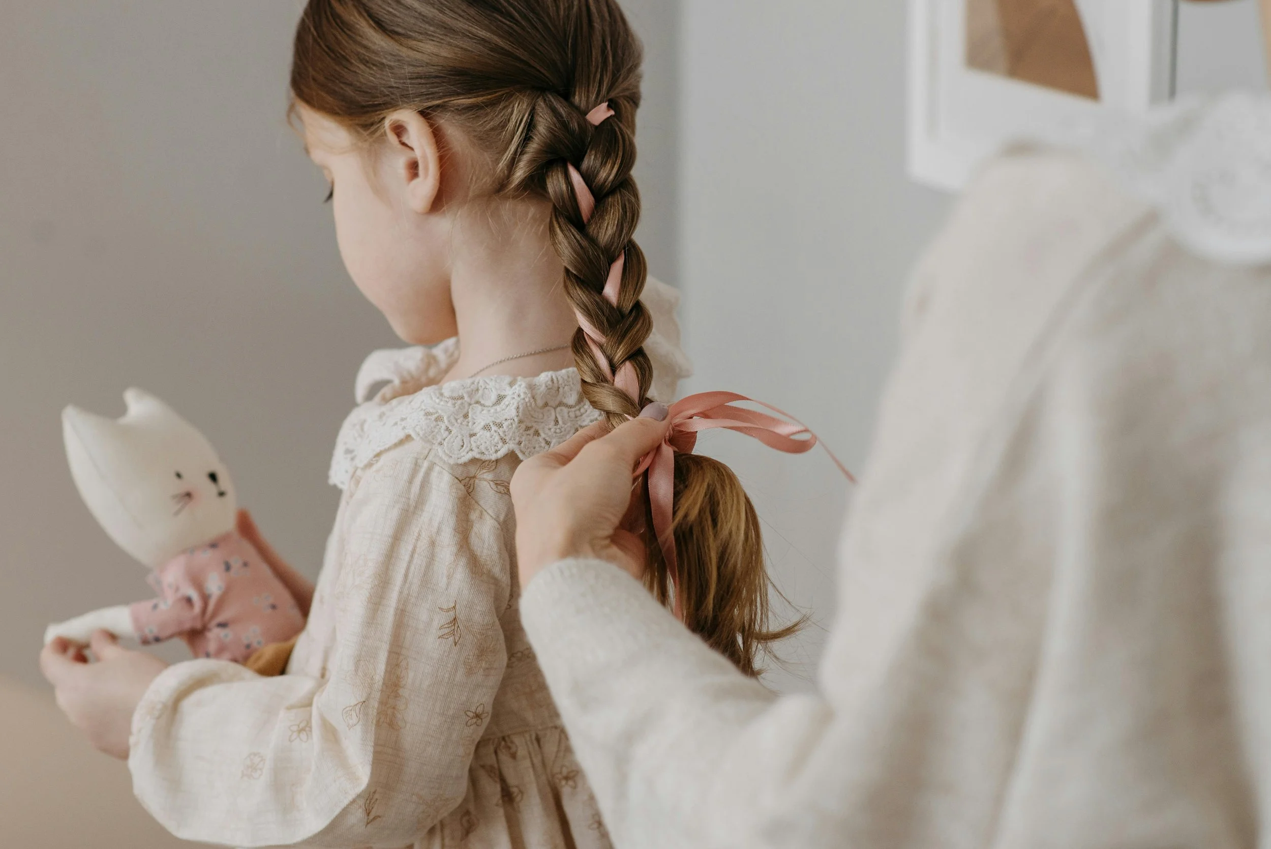 someone is braiding a young girls hair while she plays with a stuffed animal