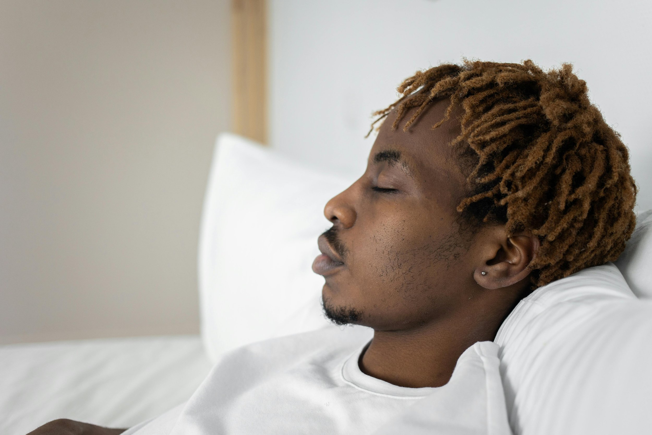 a young man is propped up against pillows on a bed with eyes gently closed