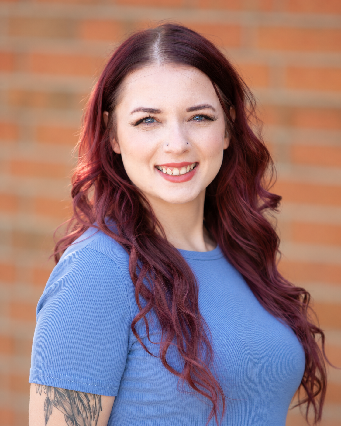 woman with long red hair standing against brick wall, smiling