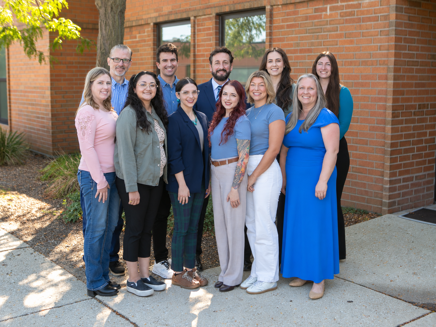 group of eleven people standing together in front of brick building smiling at the camera, all wearing varying shades of blue