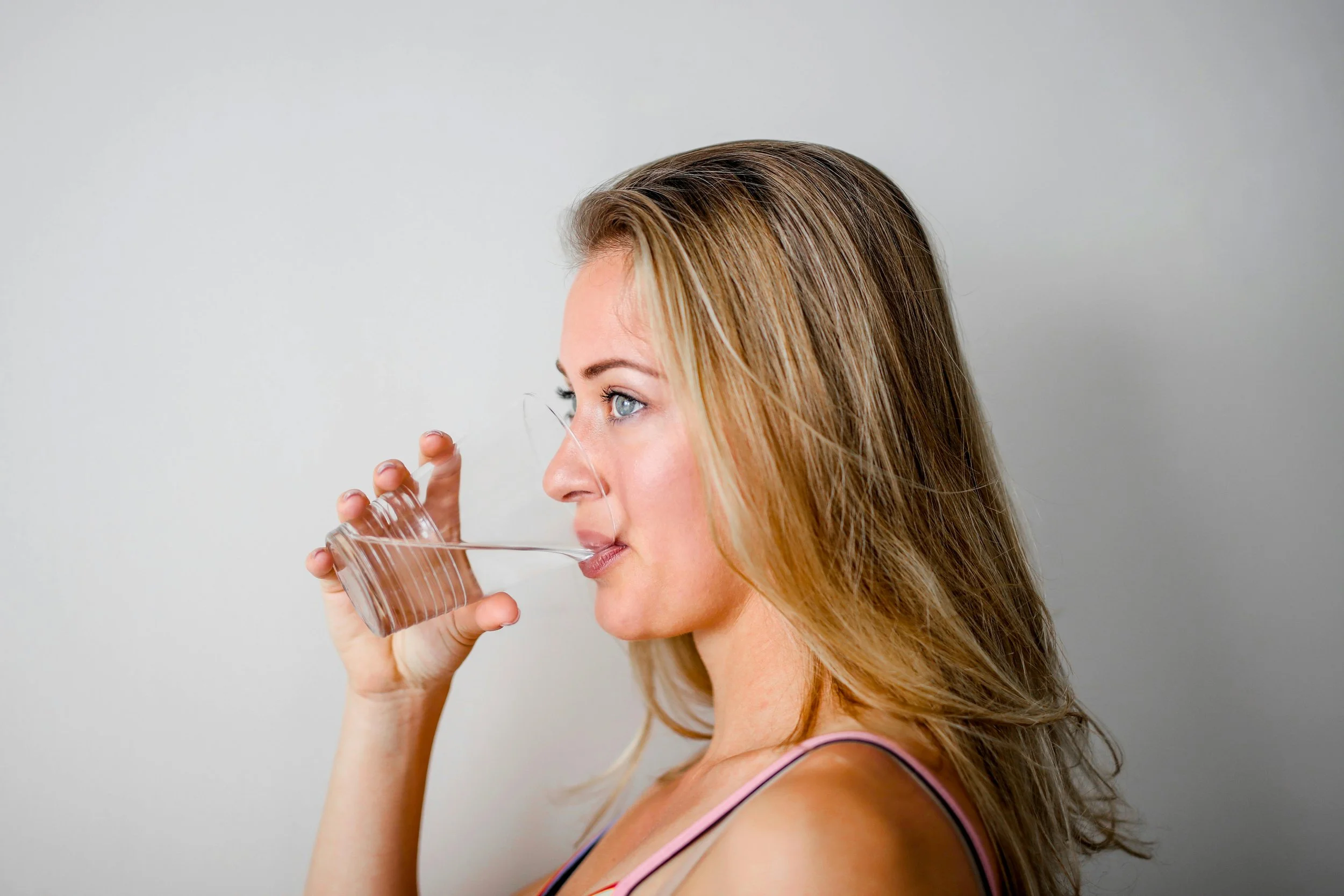 a woman with long blong hair is drinking water and looking straight ahead