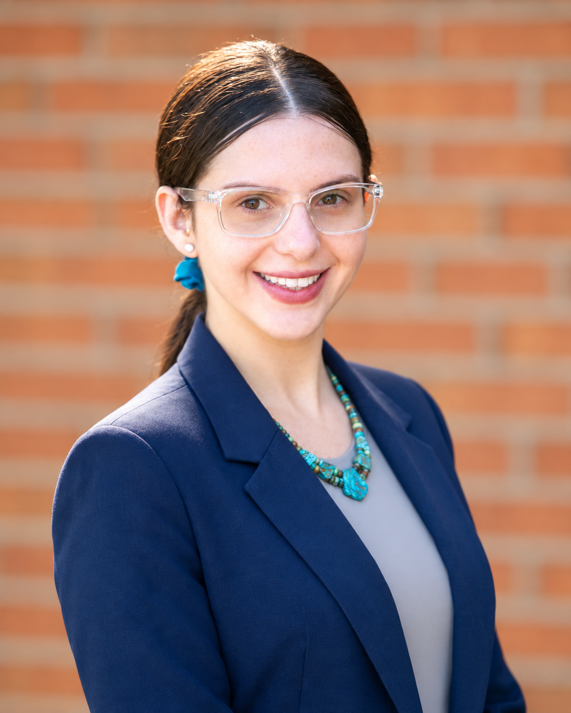 headshot of woman with long dark hair and white blazer smiling