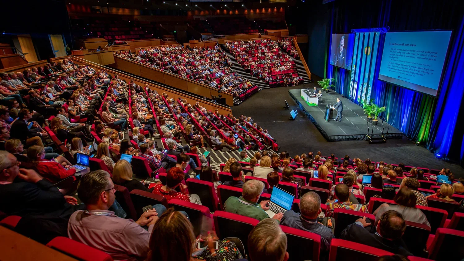 Large industry conference photographed at Brisbane Convention & Exhibition Centre with delegates watching a keynote speaker presentation.