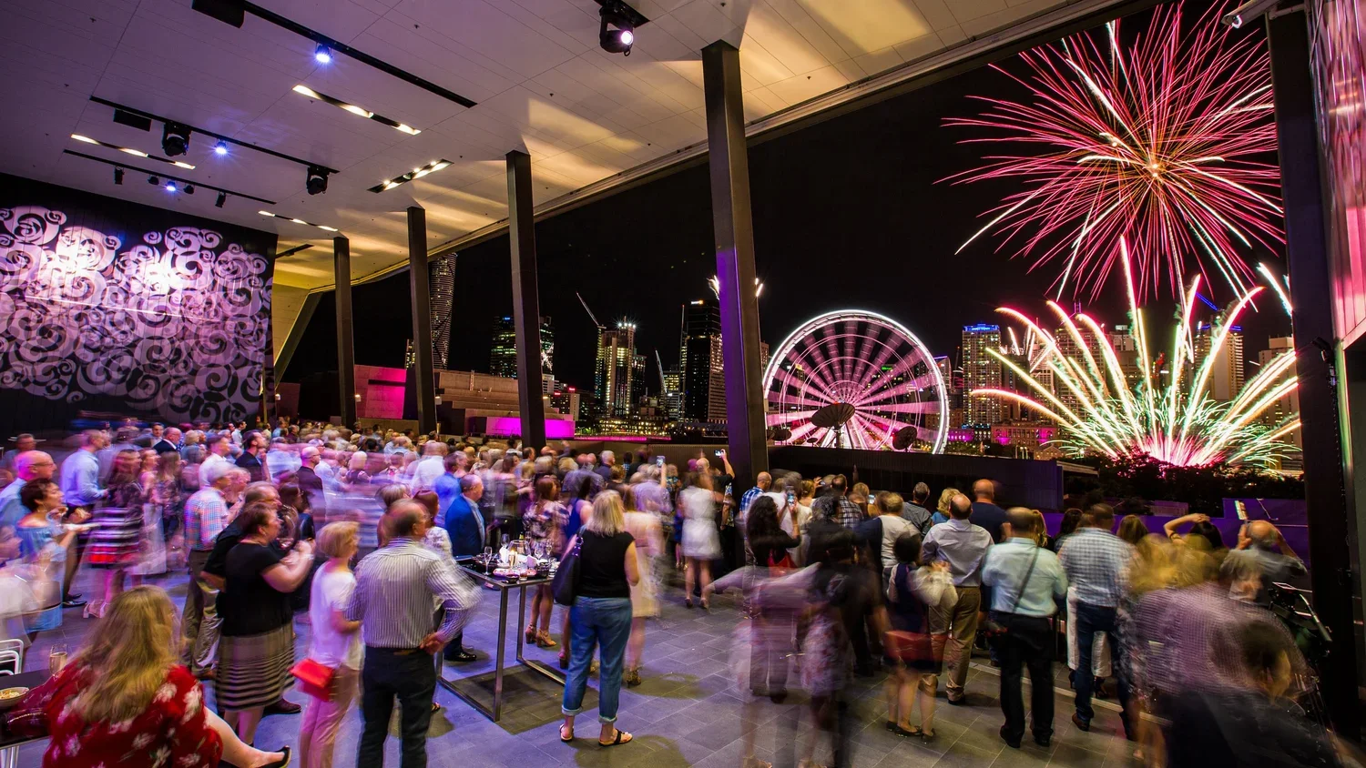 Guests networking at a large evening corporate event at the Brisbane Convention & Exhibition Centre Sky Room Terrace with entertainment, fireworks and event lighting.