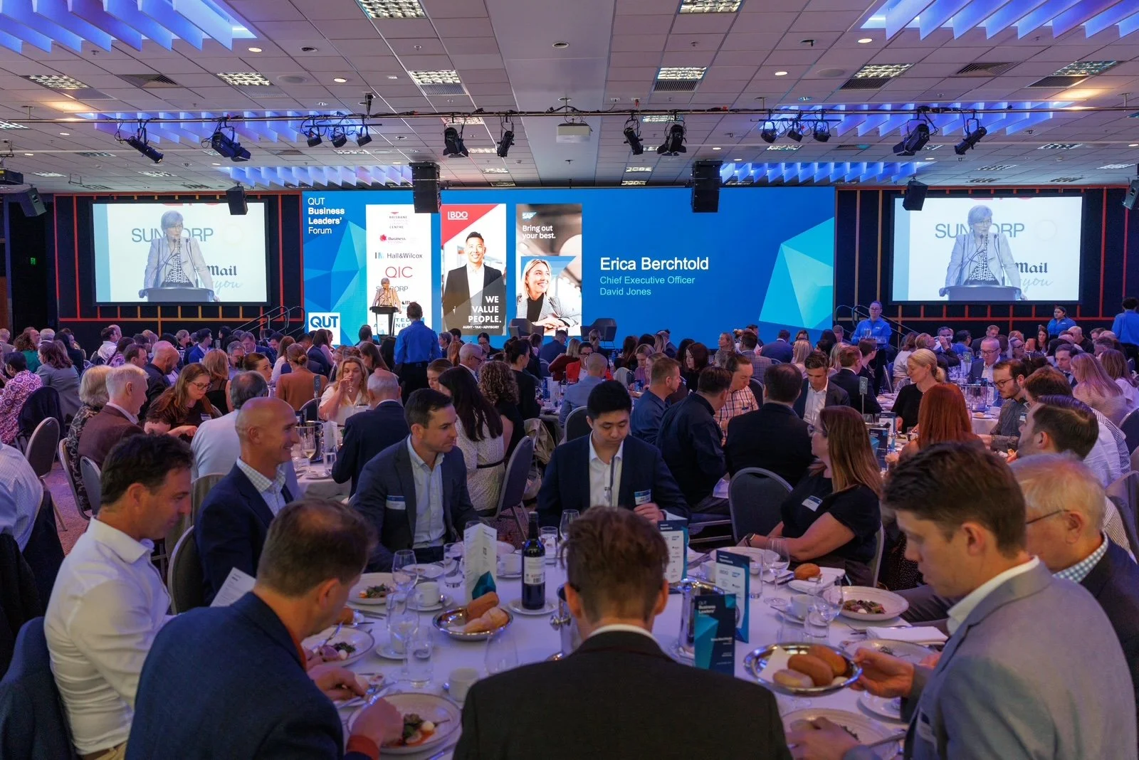 QUT Business Leaders’ Forum 2026 in the Plaza Terrace Room at Brisbane Convention & Exhibition Centre, with guests seated at round tables and a speaker presenting on stage, large screens and QUT signage.