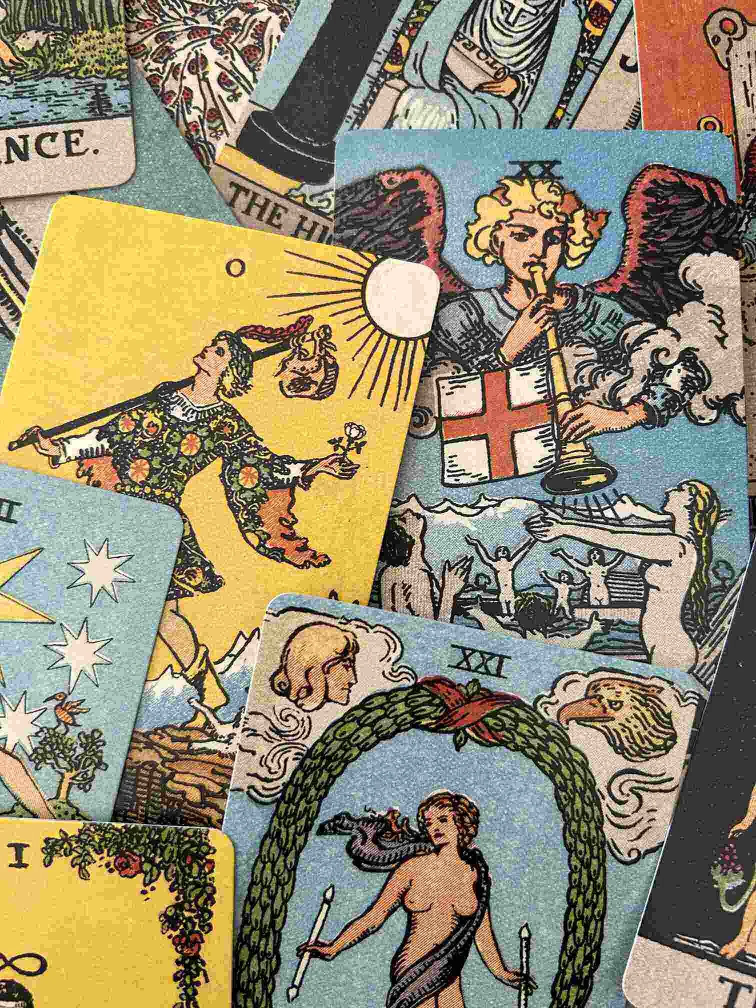 A person's hand holding the Sun tarot card over a table with various tarot cards laid out, including The Empress, The Hierophant, The High Priestess, The Strength, and others, with additional cards and tarot decks surrounding them.