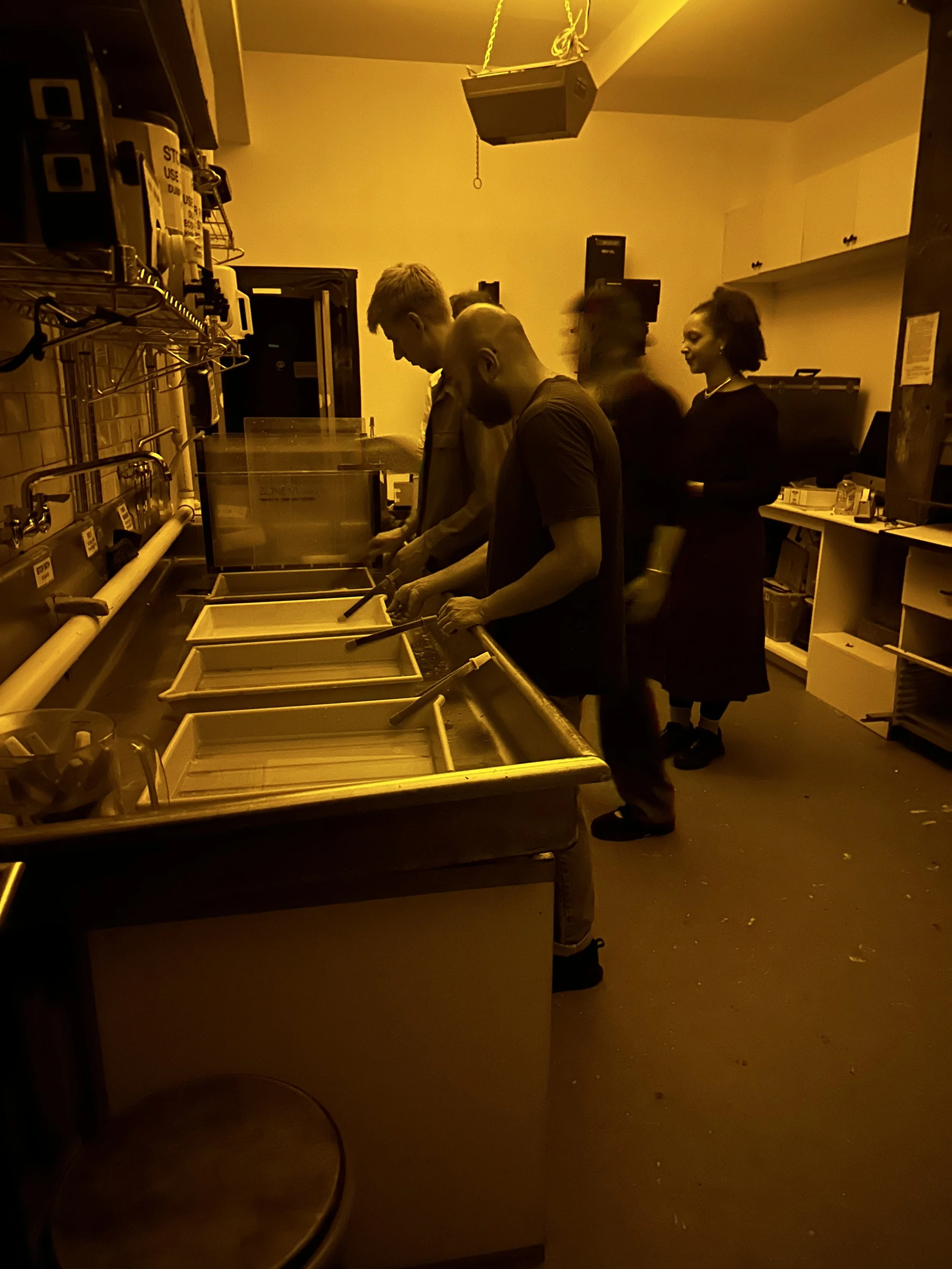 Four people developing prints in a darkroom