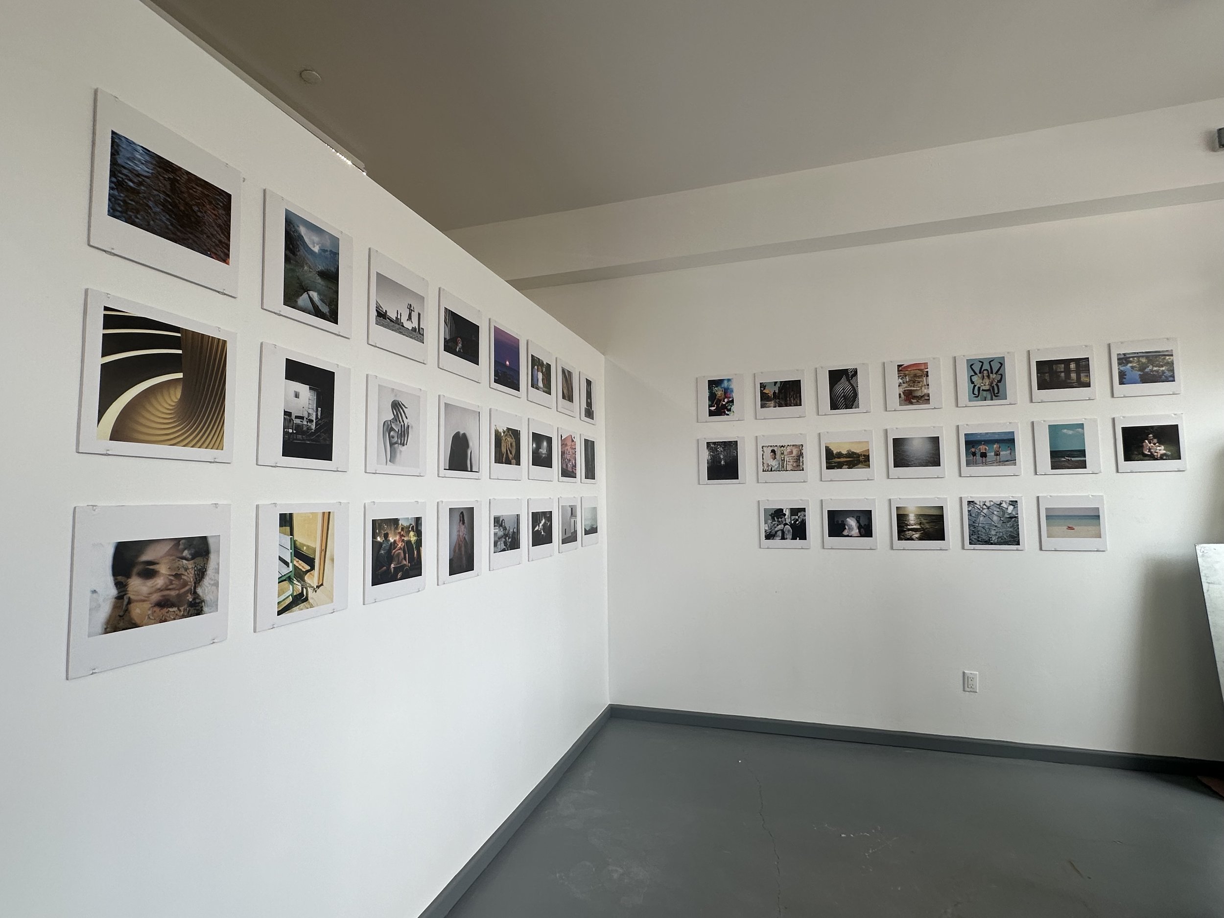 Gallery wall with multiple framed photographs on white walls in an art exhibit space.