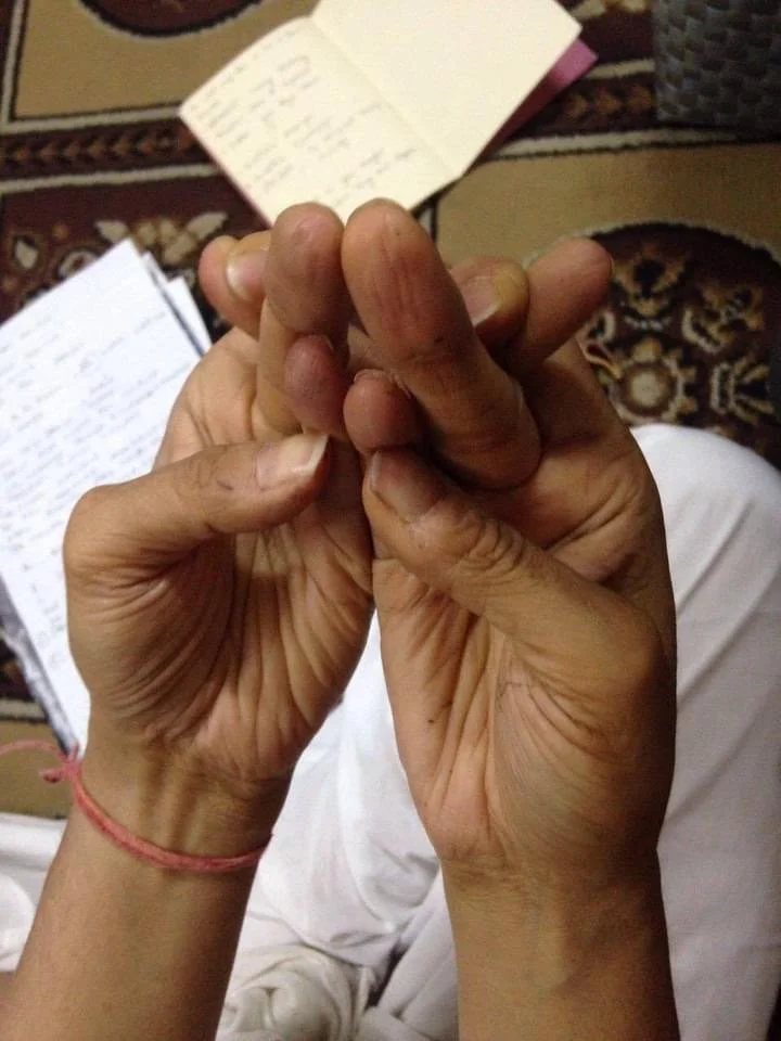 Hands in a mudra gesture with notebook in background on a patterned surface.