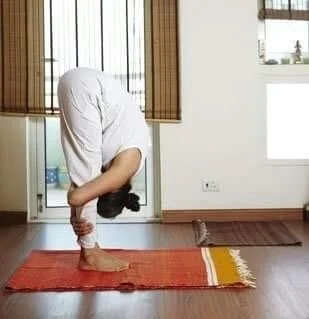 Person practicing yoga in a forward bend pose on an orange mat indoors