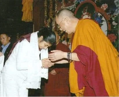 A person in traditional monk robes interacting with another person in a ceremonial setting, exchanging gestures of respect and greeting.