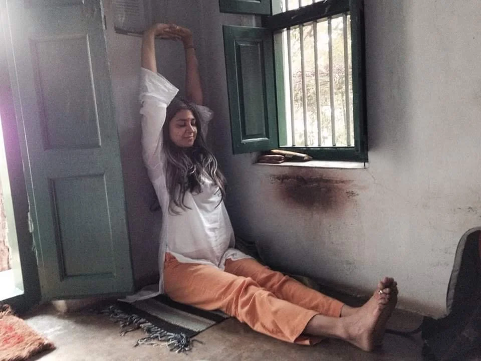 Person sitting on floor stretching arms upward near open window in relaxed pose