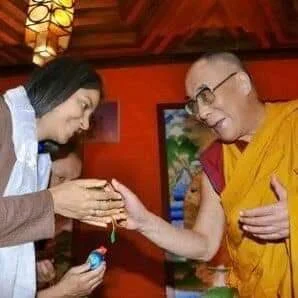 A person in traditional robes interacting with another person holding an object in a colorful setting.