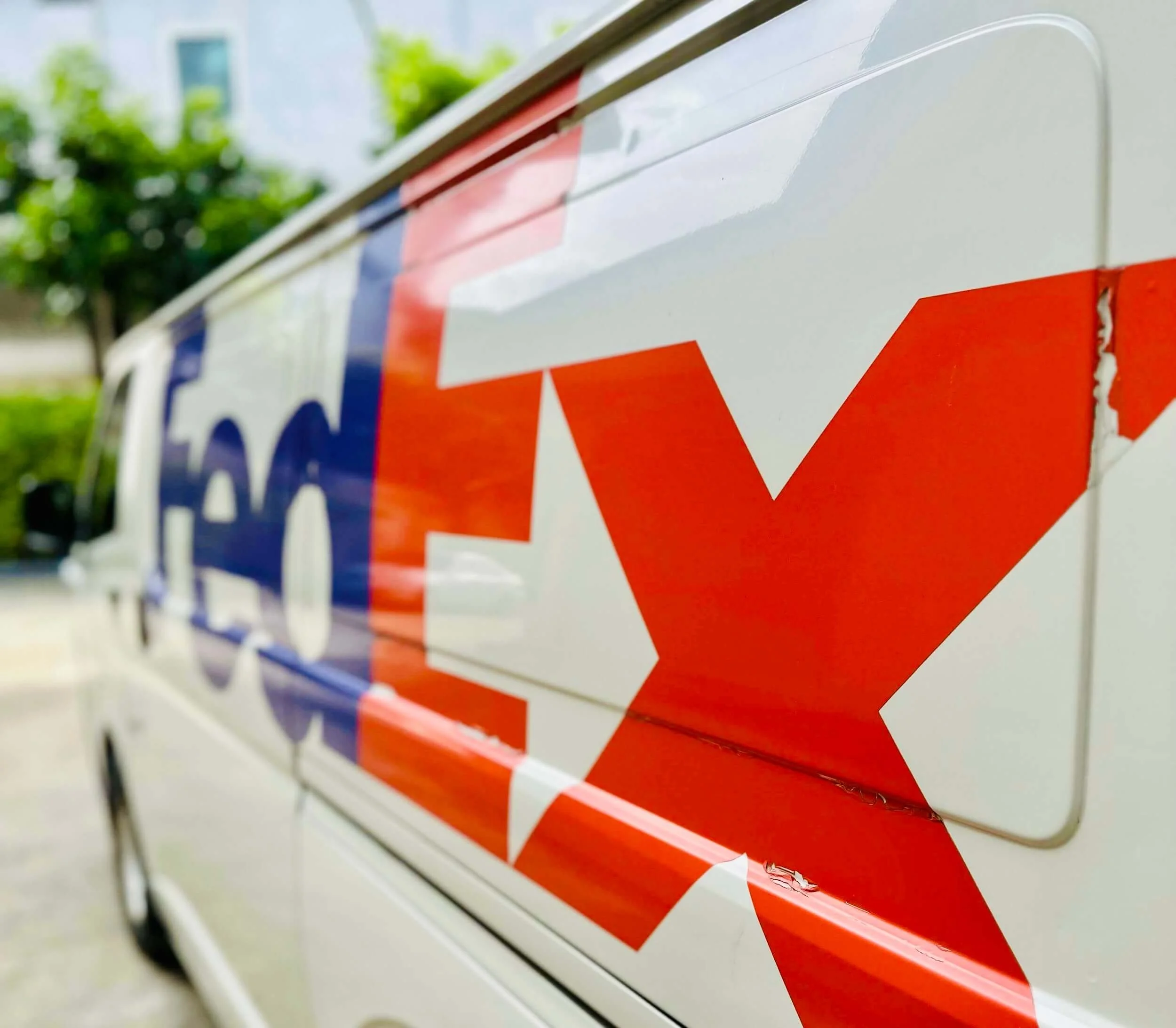 Close-up of a white vehicle with a partially visible FedEx logo in red and blue, with a noticeable small scratch on the red part of the logo.