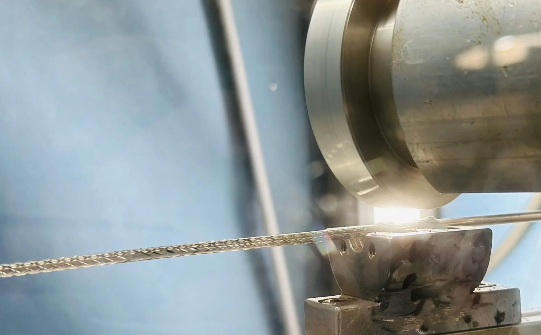 Close-up of a metal machining process with a spinning cylindrical tool shaping a metal rod, in an industrial setting.