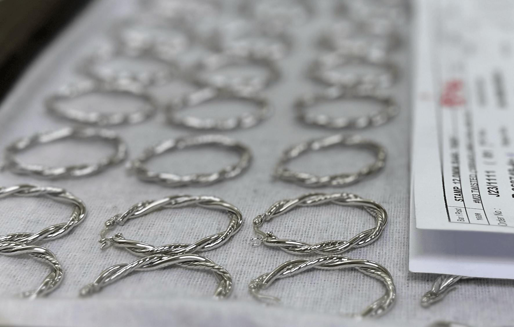 Silver twisted hoop earrings laid out on white fabric with a shipping label visible on the right side.