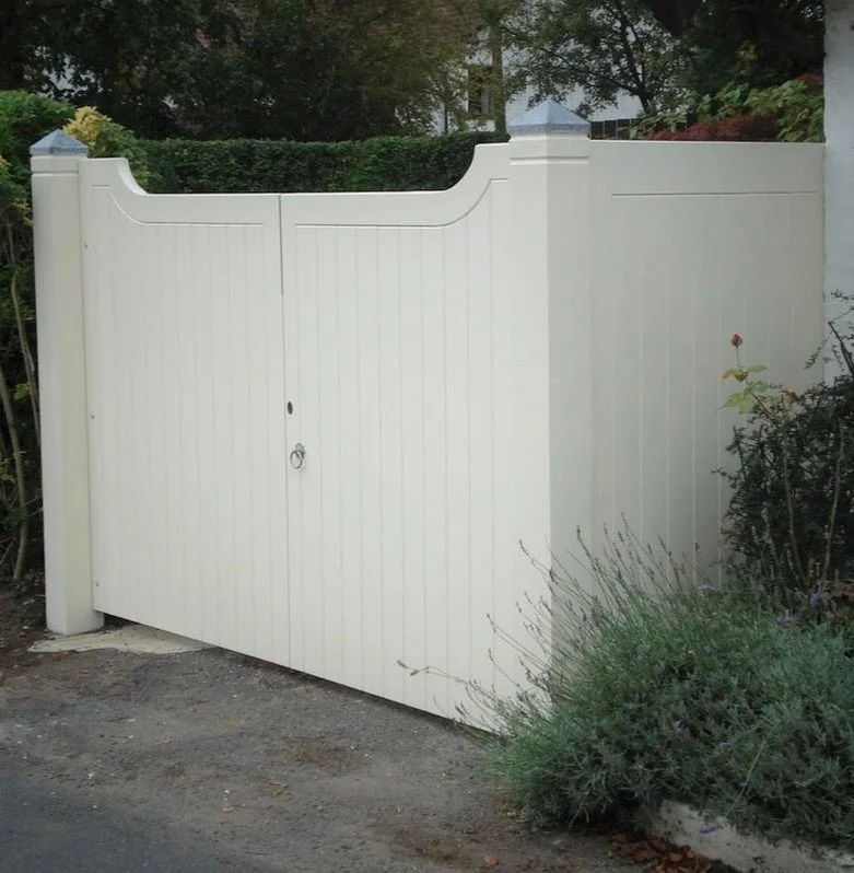 White gate with a latch in front of a garden and trees.
