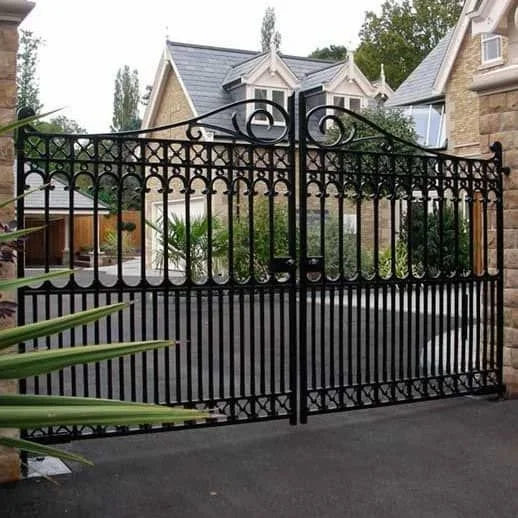 Black wrought iron gate in front of a suburban house with light-colored stone and a gable roof.