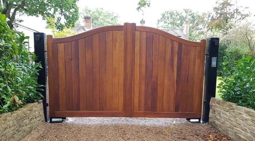 Wooden gate with an arched top, set between brick wall planters with greenery on each side.