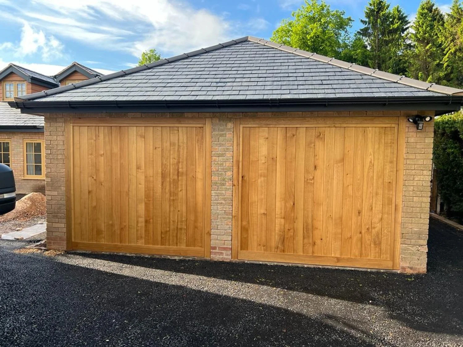 A garage with wooden doors and a brick exterior, surrounded by trees and a cloudy sky.