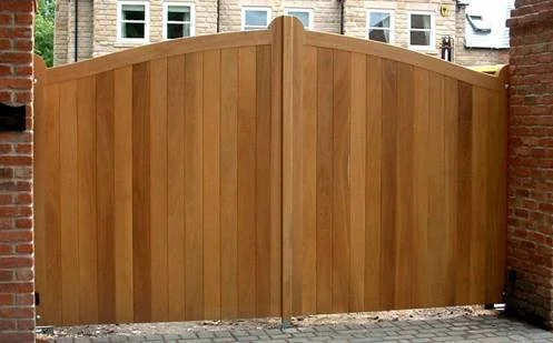 A wooden gate with a curved top, set between brick walls in an alley or backyard.
