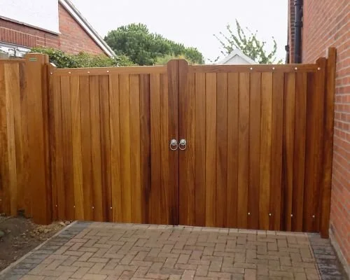 Wooden double gate with metal handles on a paved pathway between brick walls.