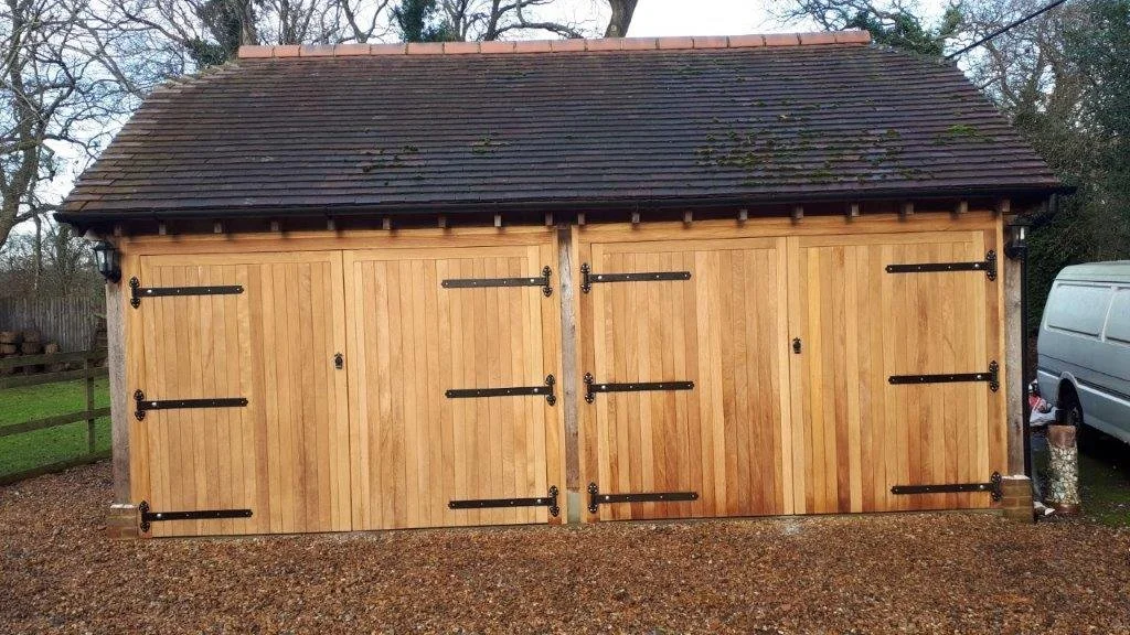 A wooden shed with vertical wood paneling, black decorative hinges, and a shingled roof. There are two large doors with black hinges and a small lock in the middle.