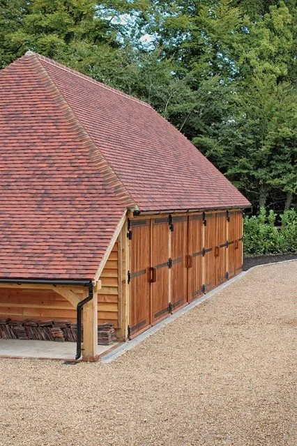 Wooden garage with a red tiled roof, surrounded by trees and a gravel driveway.