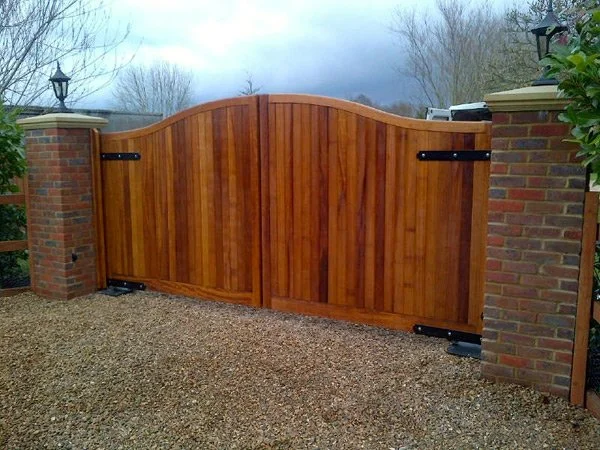 Wooden double gate attached to brick pillars in an outdoor setting with cloudy sky overhead