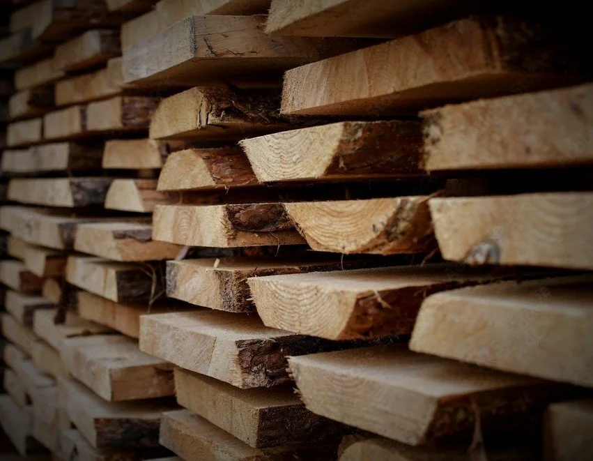Stacked pieces of cut lumber arranged in a neat pile, with visible wood grain and some bark on the edges.