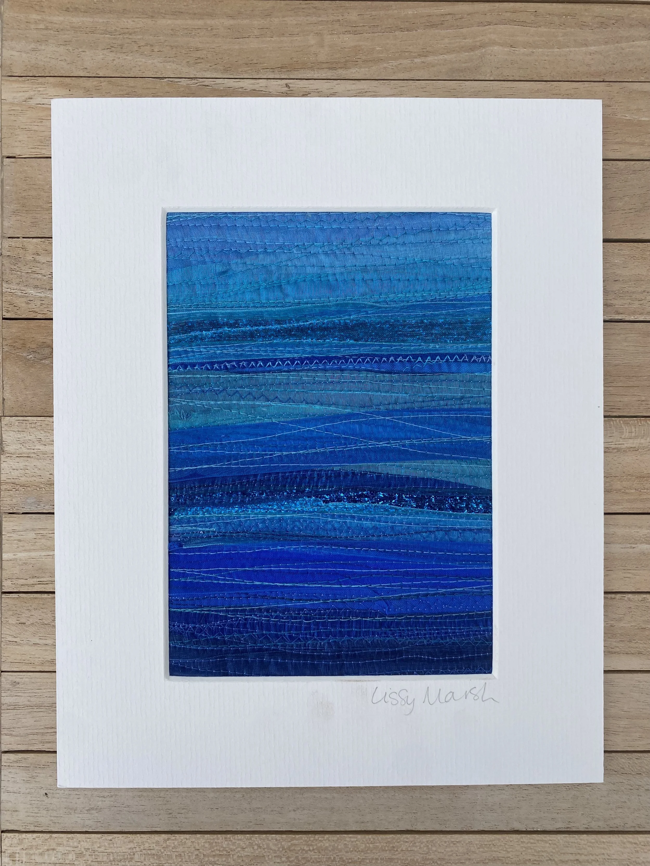Textured abstract artwork with shades of blue stitched in horizontal layers, matted on a white background, signed at the bottom right.