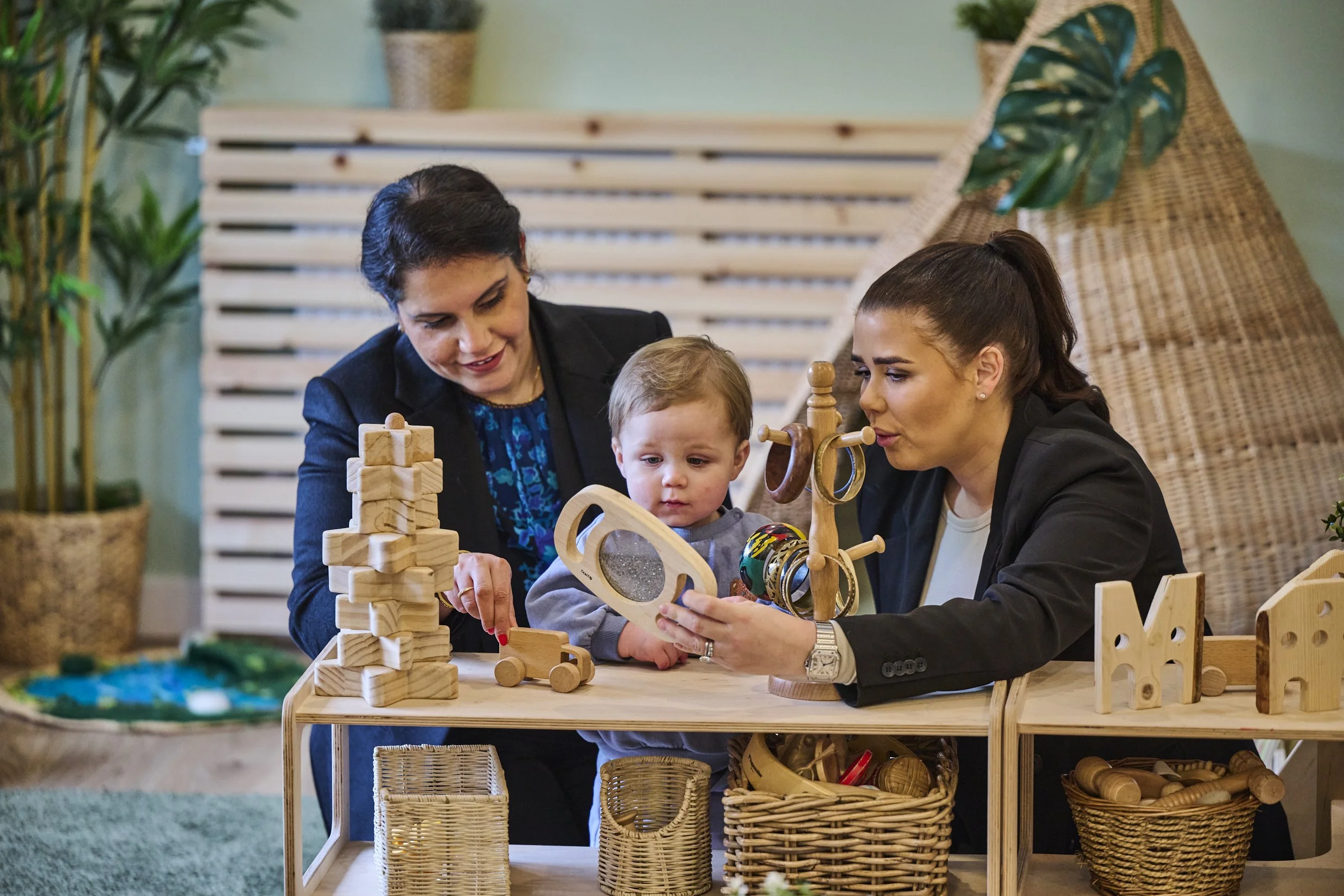 Photo of two female adults in a nursery playing with a toddler and his toys