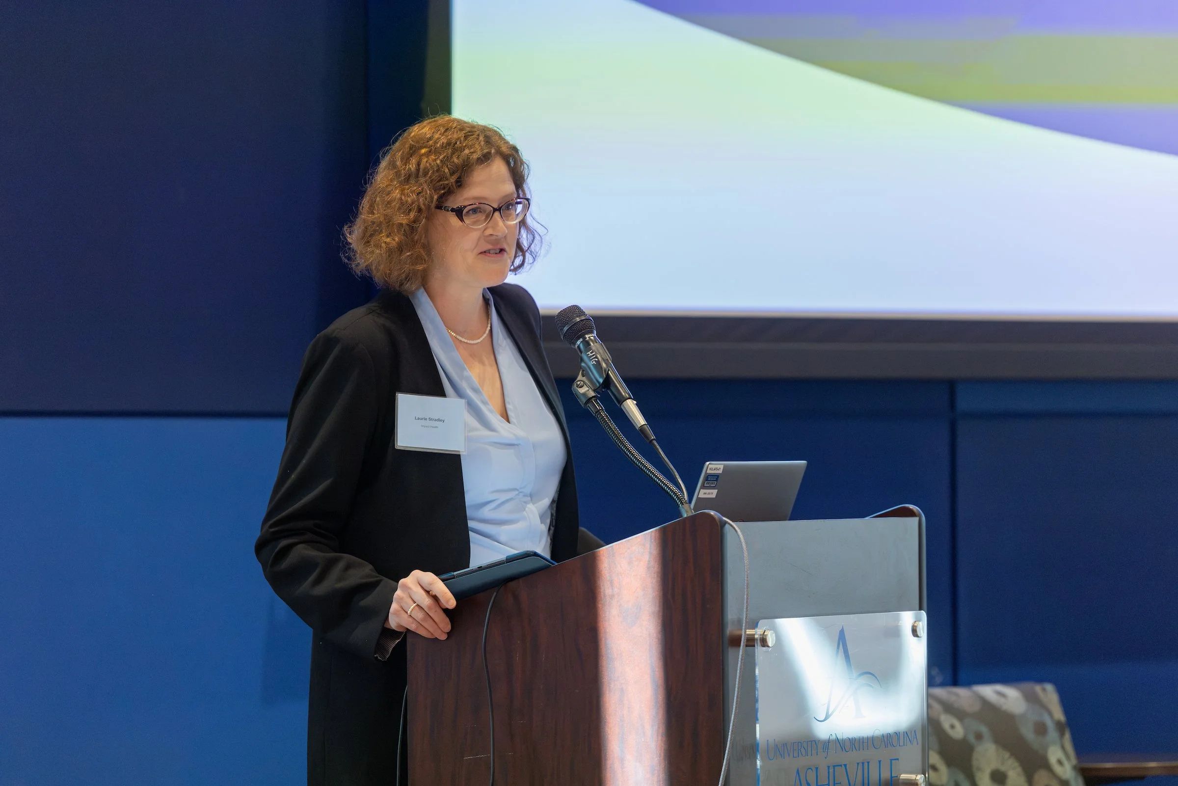 Laurie Stradley stands behind a podium in a light blue shirt and darker blazer.