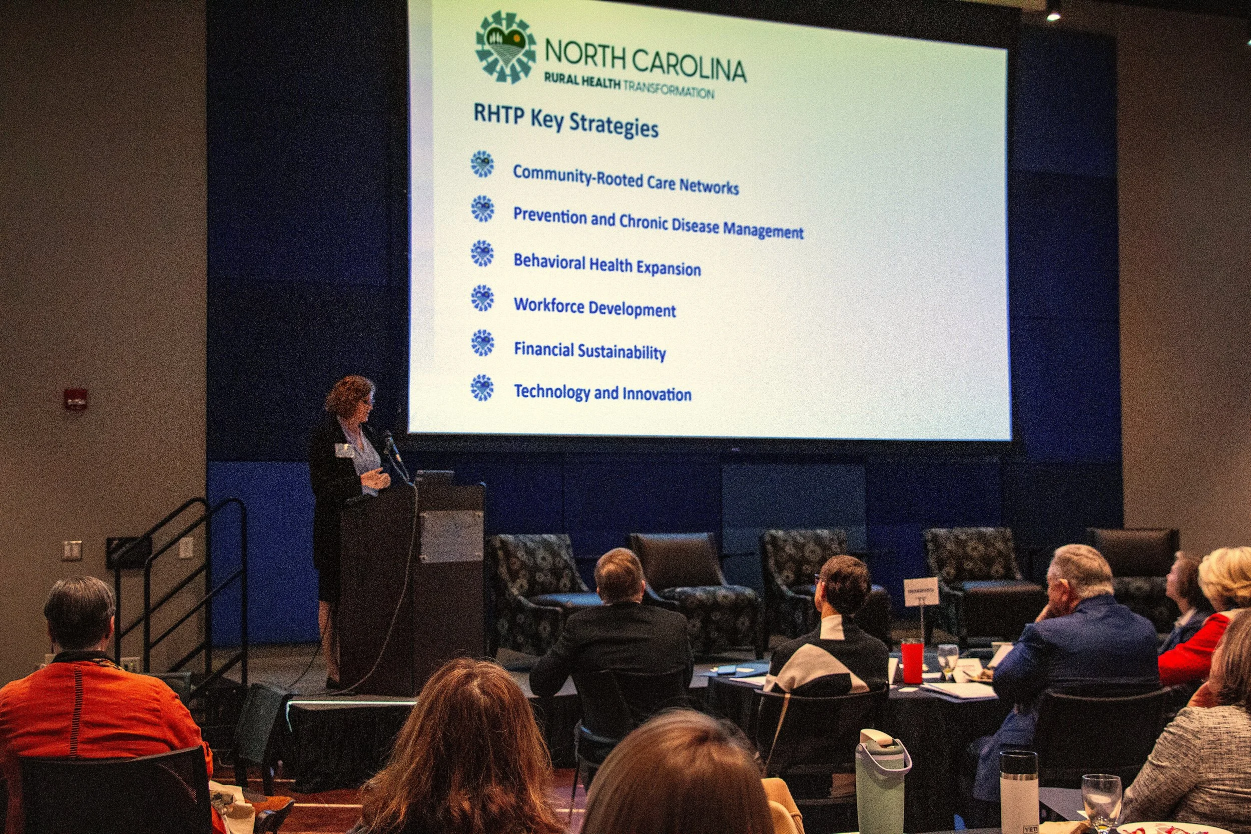Laurie Stradley (CEO, Impact Health) delivers keynote address “Transforming for Resilience: How Western North Carolina is Reimagining Rural Health.” Showing Rural Health Transformation slide. Photo credit: Michaela Lumpert, Impact Health. 