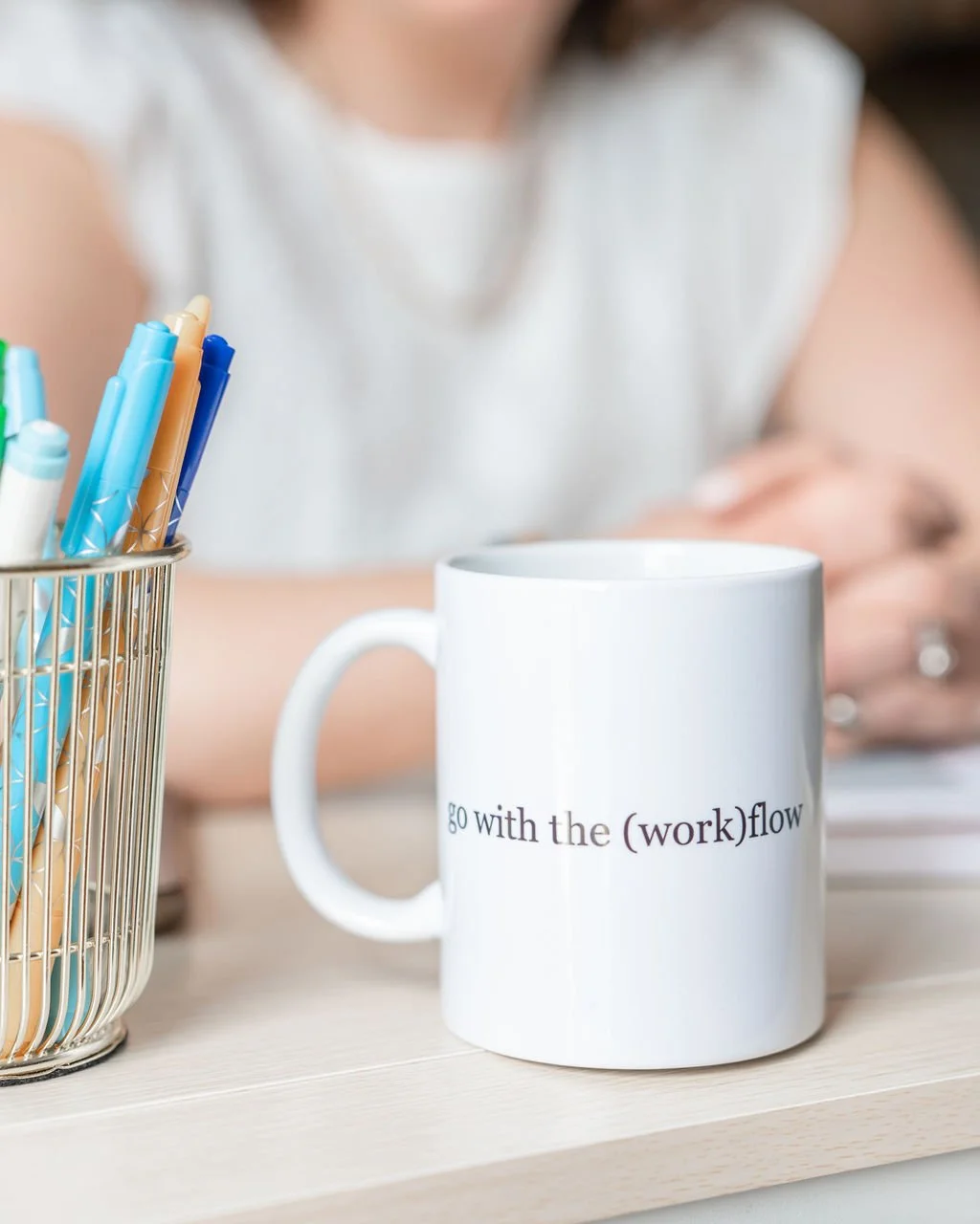 White coffee mug with 'go with the (work)flow' text, sitting on a desk with pens and planning tools.