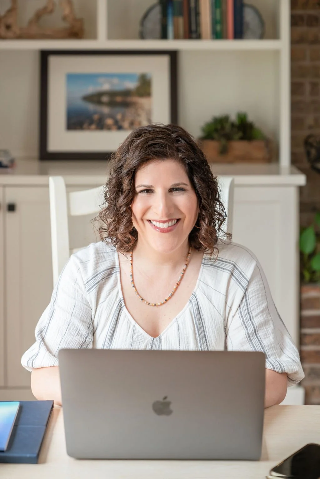 Productivity coach sitting at a desk and working on a laptop in a bright home office.
