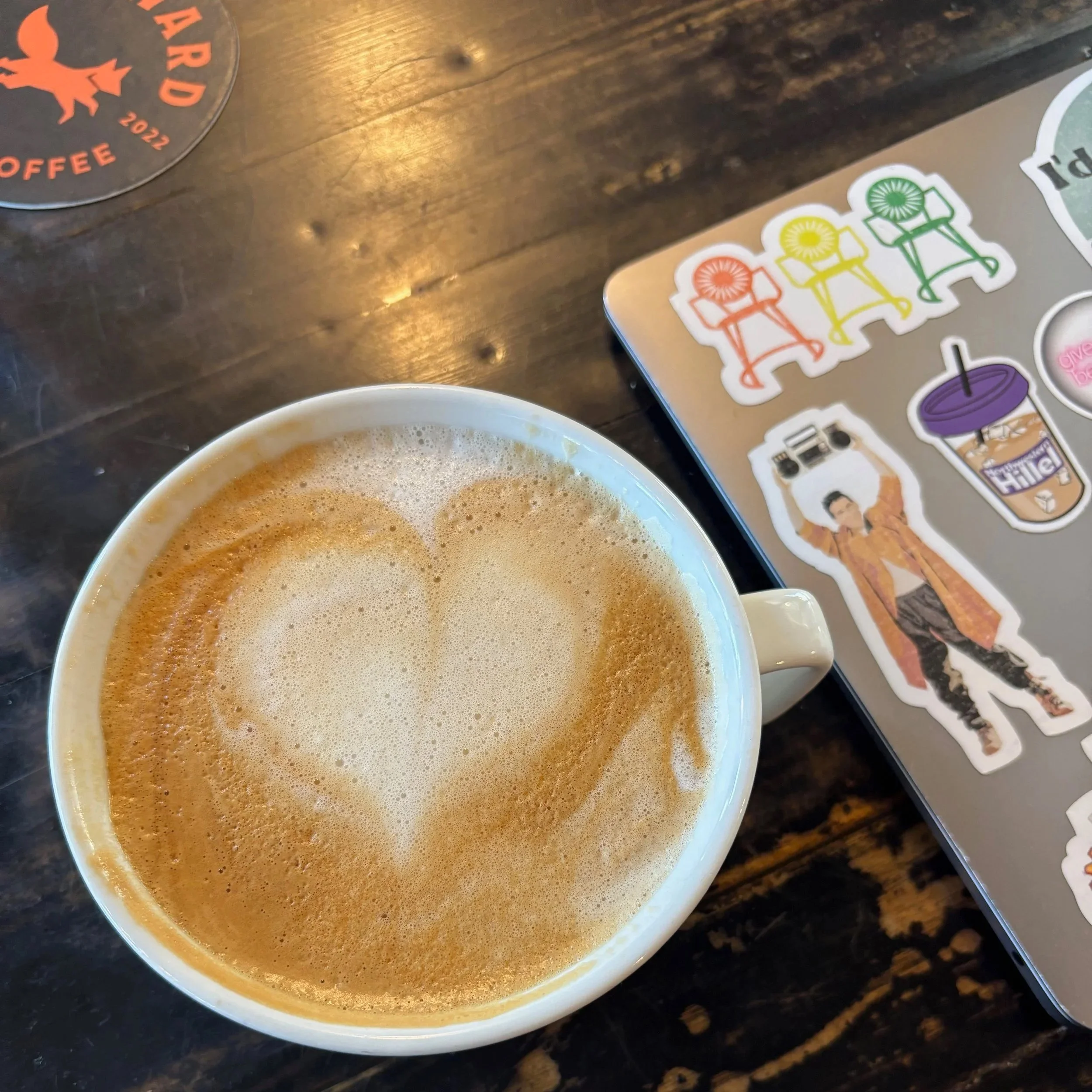 Coffee on a table next to a laptop with productivity-themed stickers, representing a casual work setup.
