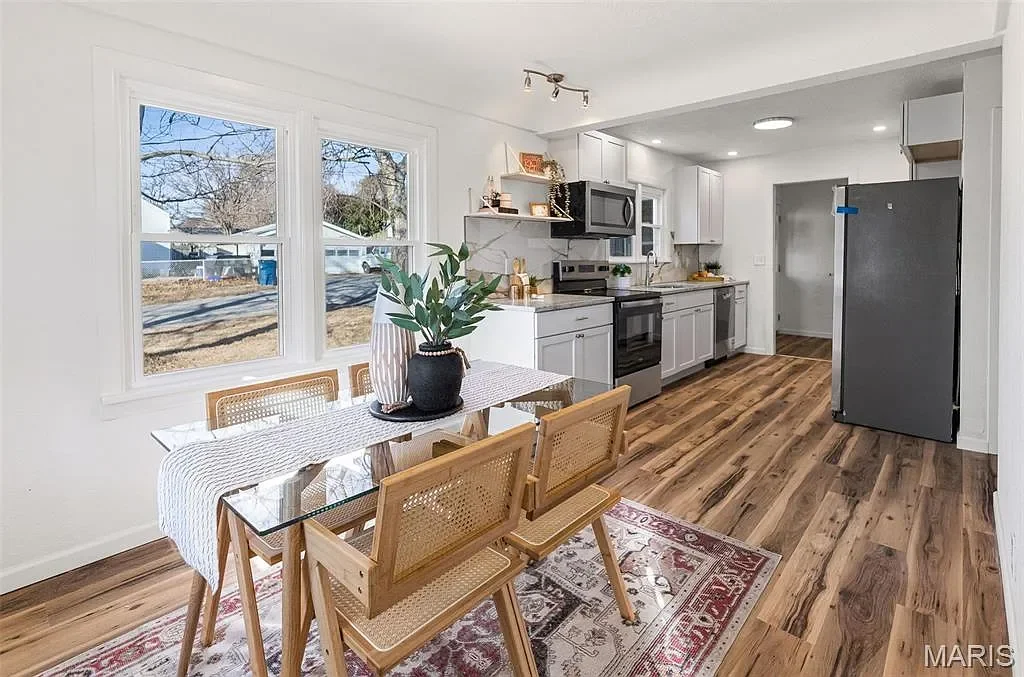 Kitchen with dining table, wooden chairs, large windows, and modern appliances including a refrigerator, oven, microwave, and dishwasher. Hardwood floors and white walls. Kitchen renovated by ASA Construction in Alton Illinois. 