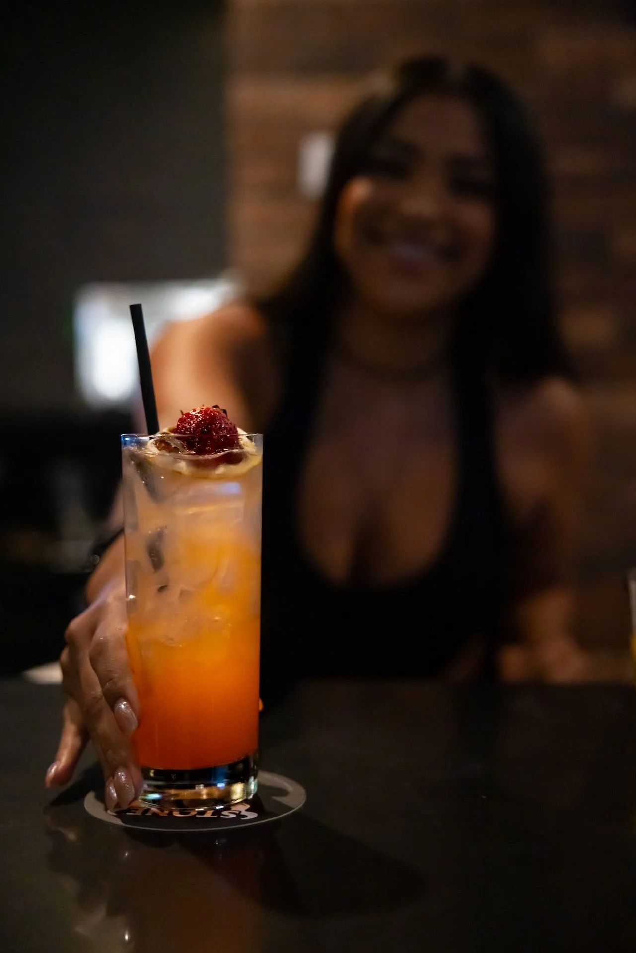 A woman holding a colorful cocktail with a cherry on top in a bar or restaurant setting.