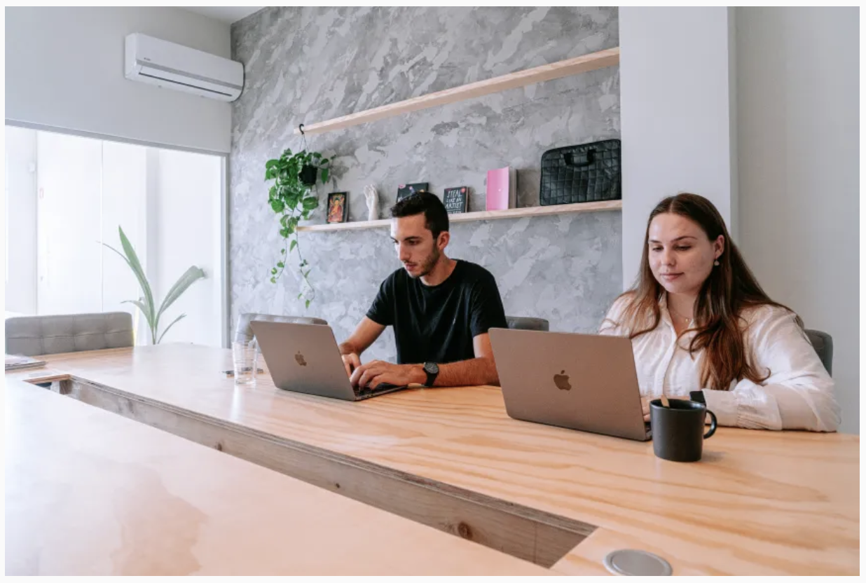 Two people working on laptops at a wooden desk inside FISGA coworking space in Porto, Portugal.