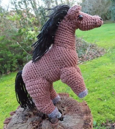 A brown crocheted horse with a black mane on its hind legs