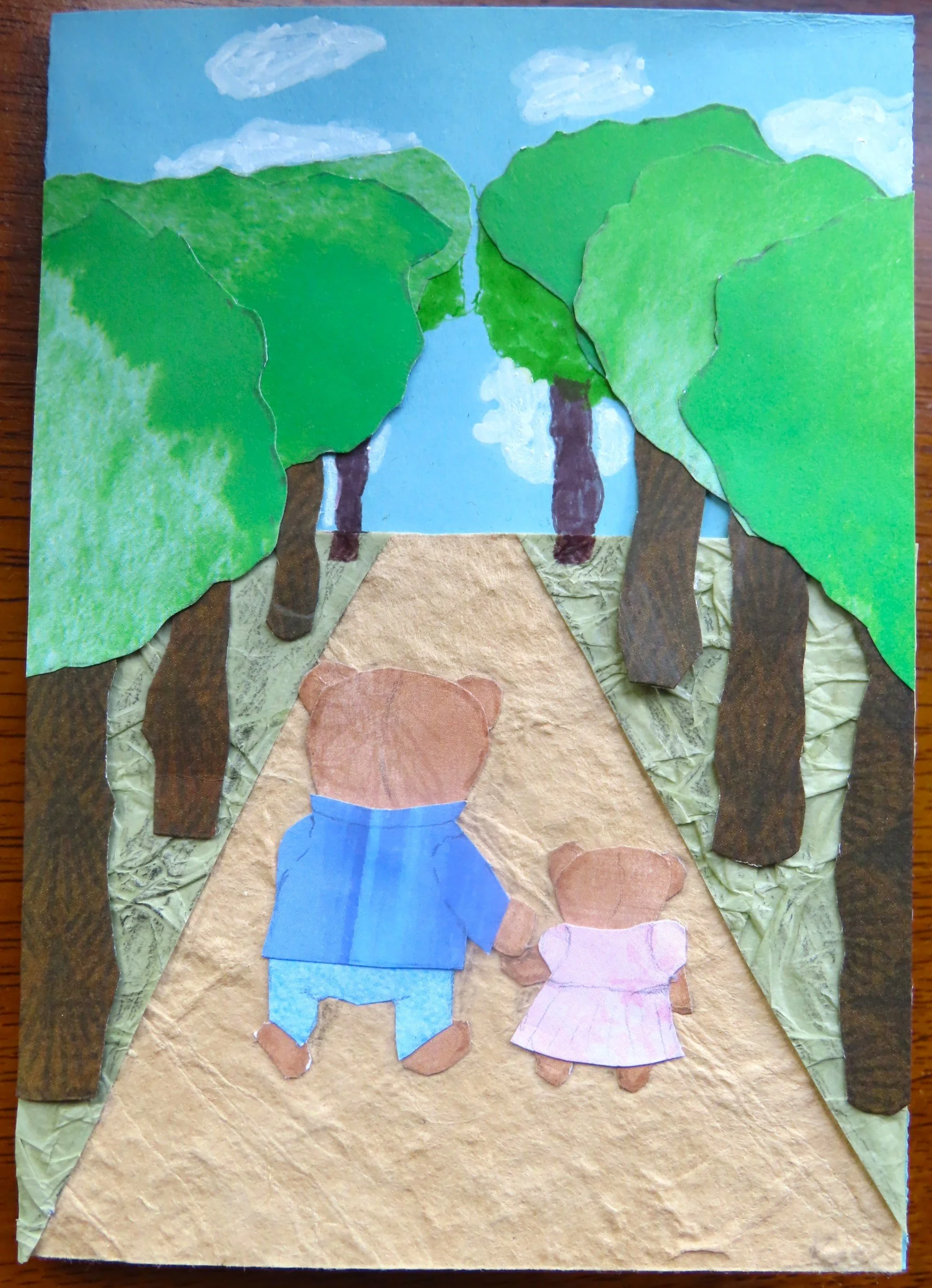 A handmade card depicting two teddy bears, a bigger one in blue shirt and trousers and a smaller one in a pink dress, viewed from behind as they walk up an avenue of trees