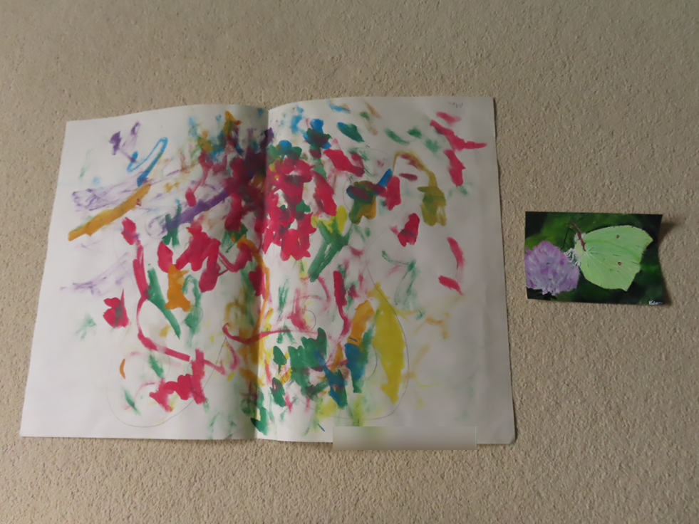 A child's painting of multicoloured blobs next to a smaller painting of a green butterfly