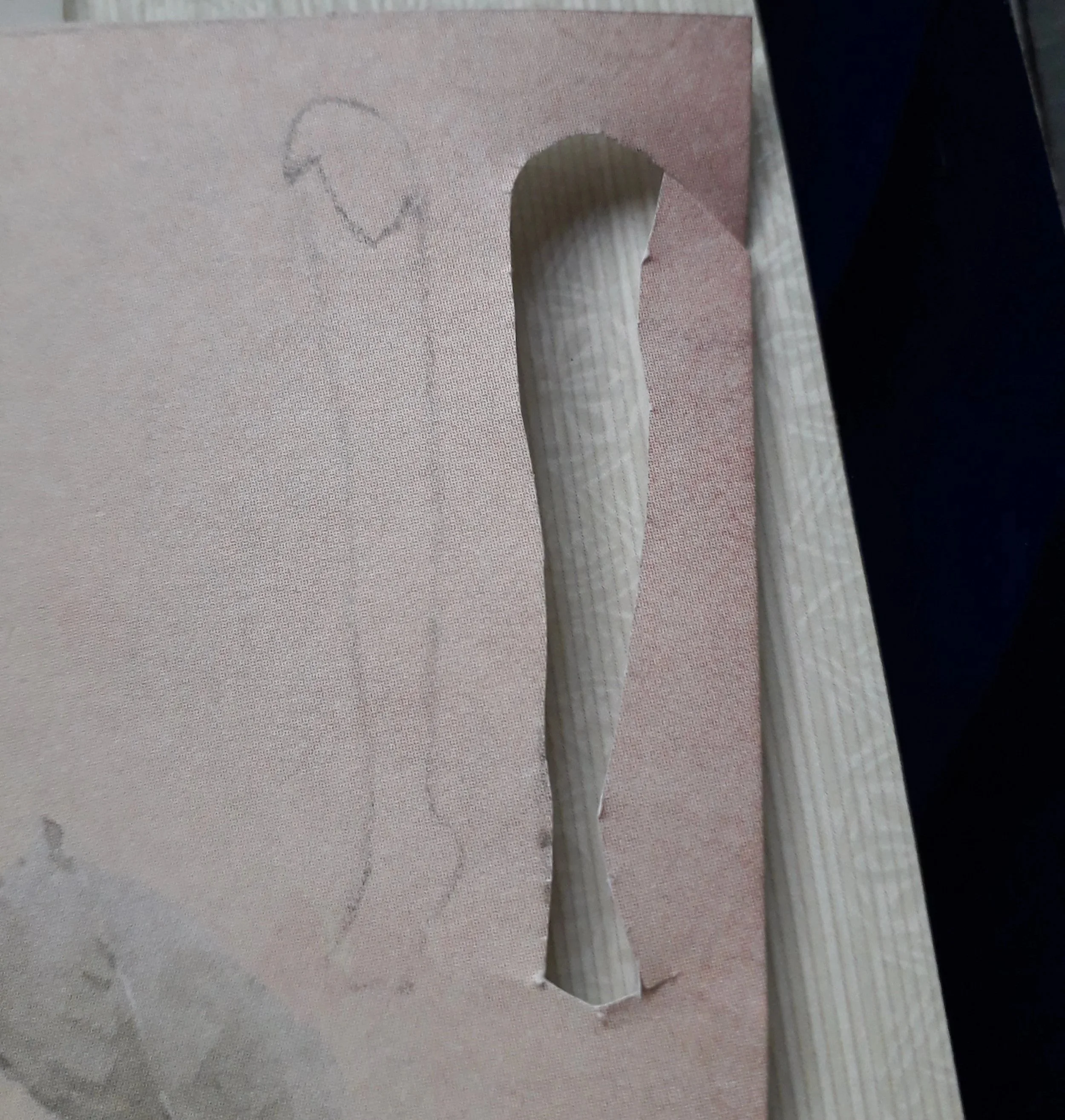A piece of peach-coloured paper with the outline of a leg drawn on it; next to the outline of a leg is a hole cut into the paper shaped like a leg