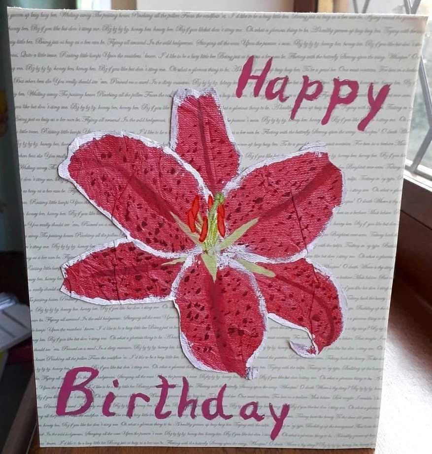 A handmade card depicting a pink lily and the words "Happy Birthday", on a green background with small cursive script
