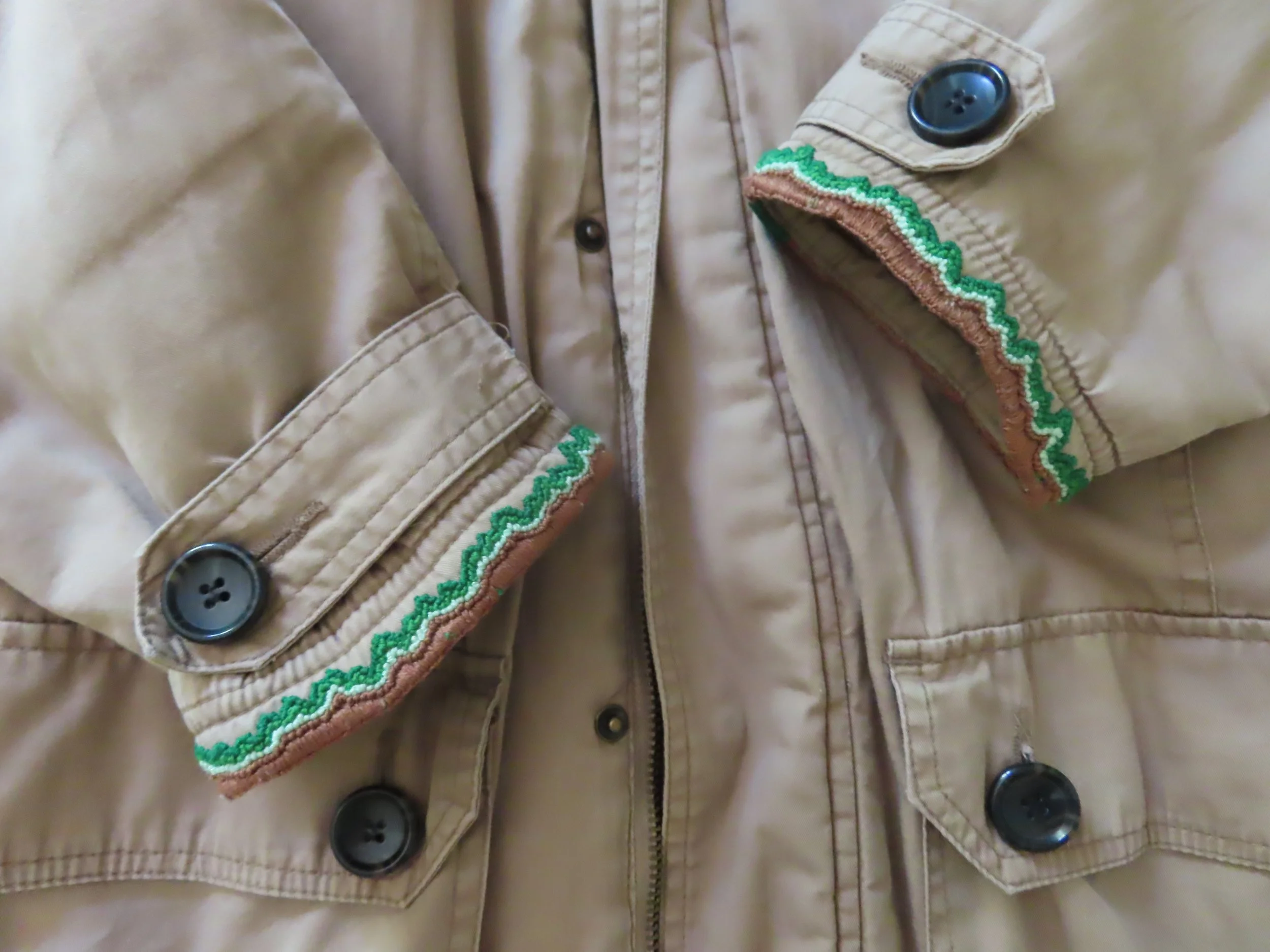 The ends of two coat sleeves with edges embroidered with greens and browns in a zigzag pattern