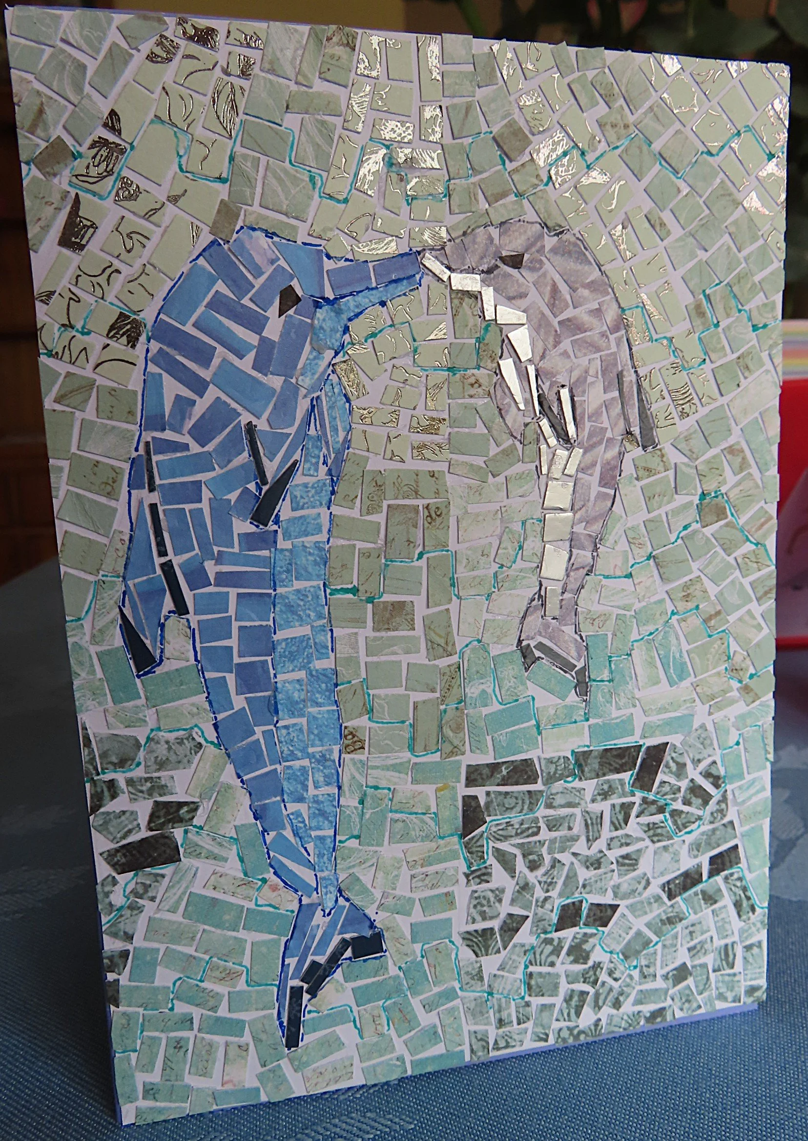 A handmade card depicting a mosaic design of a mother and baby dolphin with noses touching