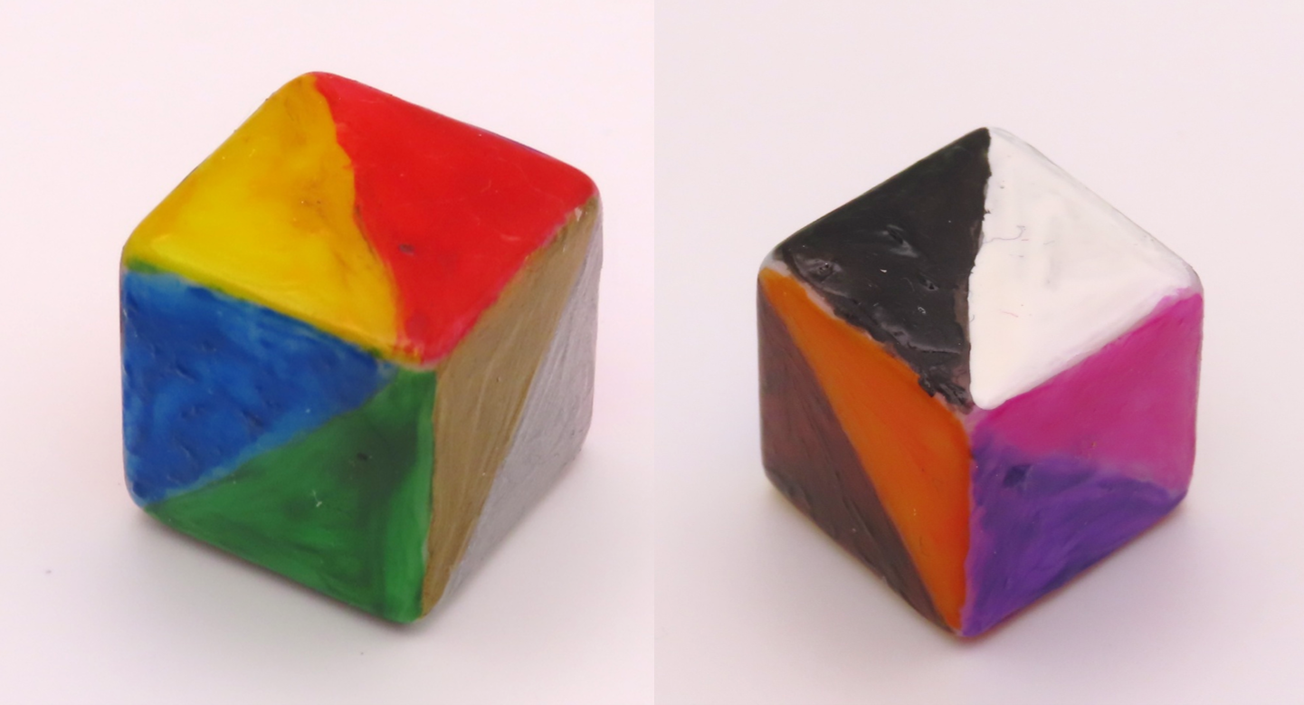 Two images of a cube-shaped die, with each face painted as two coloured triangles; red and yellow, blue and green, silver and gold, black and white, orange and brown, purple and pink