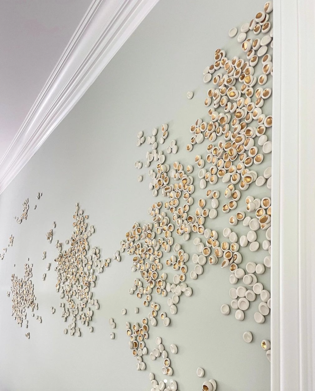 Decorative world map made of white and gold circular ceramic pieces on a light green wall.